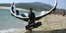 Deportista portando un parapente y una tabla de kitesurf