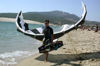 Deportista portando un parapente y una tabla de kitesurf