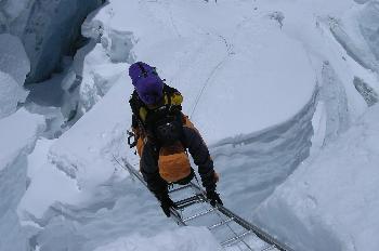 Escalador cruzando una grieta en un glaciar con una escalera