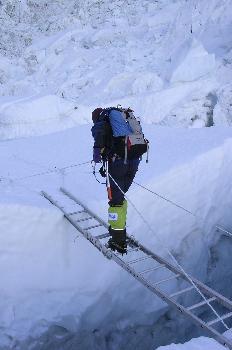 Escalador cruzando una grieta en un glaciar con una escalera